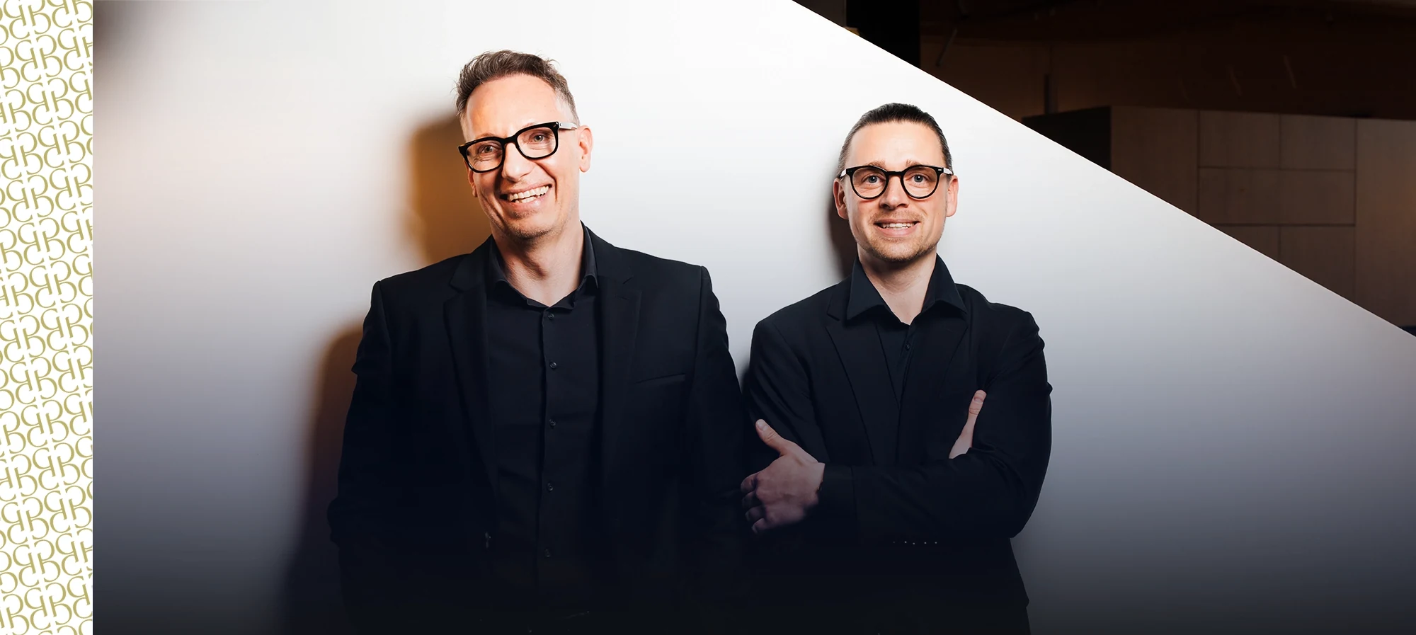 Roman und Georg stehen lächelnd vor einer weißen Wand
